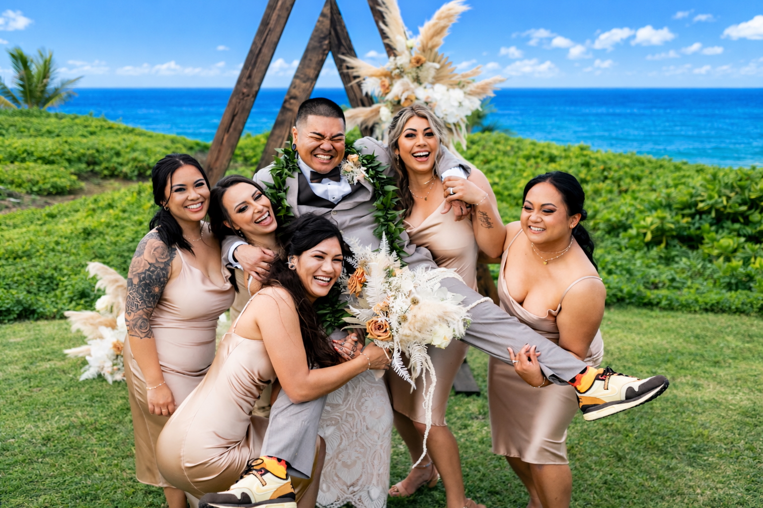 Wedding party smiling together on the oceanfront lawn in front of the ceremony arch