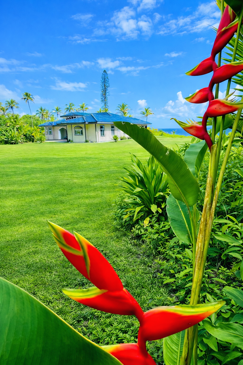 Red heliconia blooms framing the estate lawn and villa with the ocean in the distance